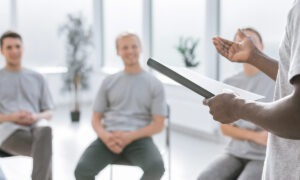 Attachment options… man reading from a notebook in front of group of men sitting