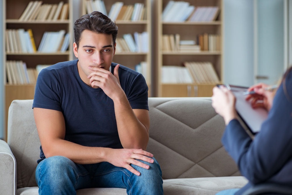 man thinking while sitting on a couch across from his therapist